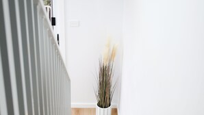 A wooden staircase with a white railing, leading to a room with a white wall and a potted plant.