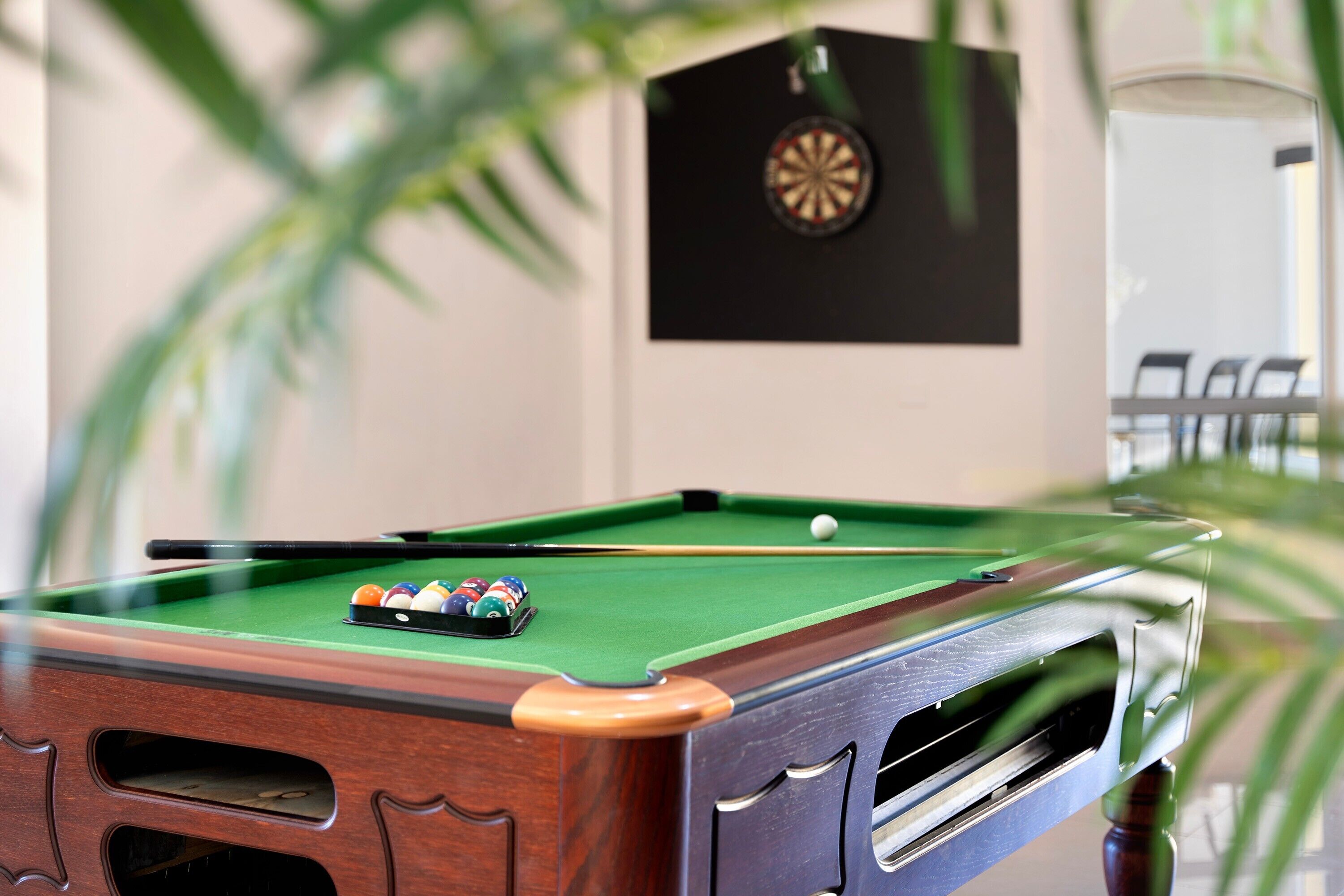 A pool table with balls, a dartboard, and a clock on the wall.