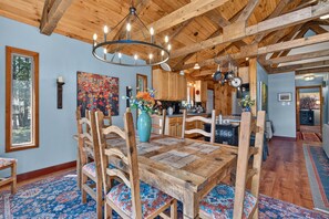 A dining area with a wooden table and chairs, a chandelier, and a colorful painting on the wall.