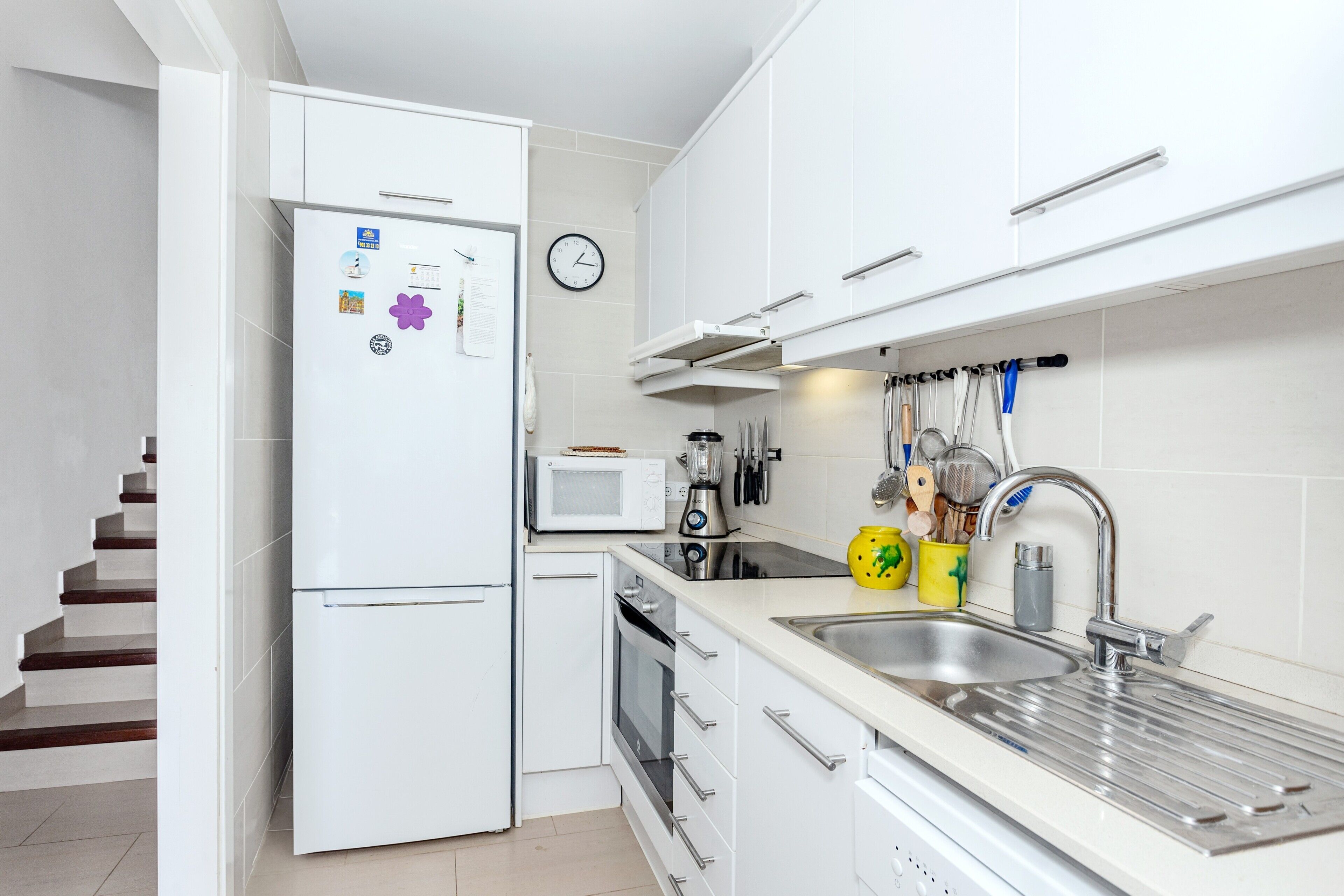 Una cocina moderna con armarios blancos, microondas, lavamanos y un reloj en la pared.