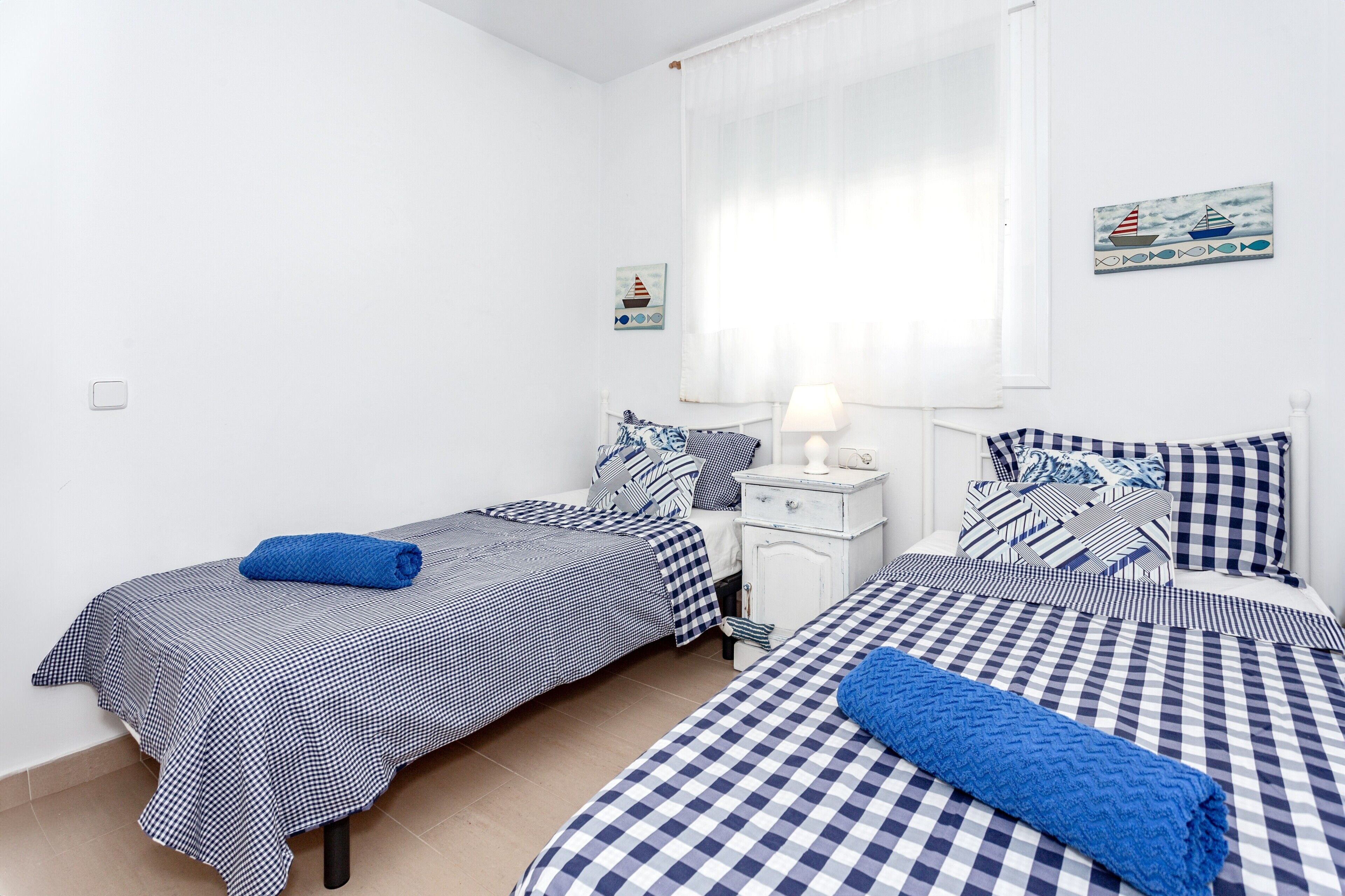 Ein Schlafzimmer mit zwei Betten, einem Nachttisch, einer Lampe und Wandbildern im Seestil.