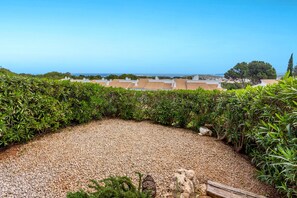 Um jardim no terraço com um caminho de cascalho, vegetação exuberante e vista para o mar e edifícios.