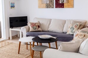 Uma sala de estar com sofá, televisão, mesa pequena e mesa de centro.