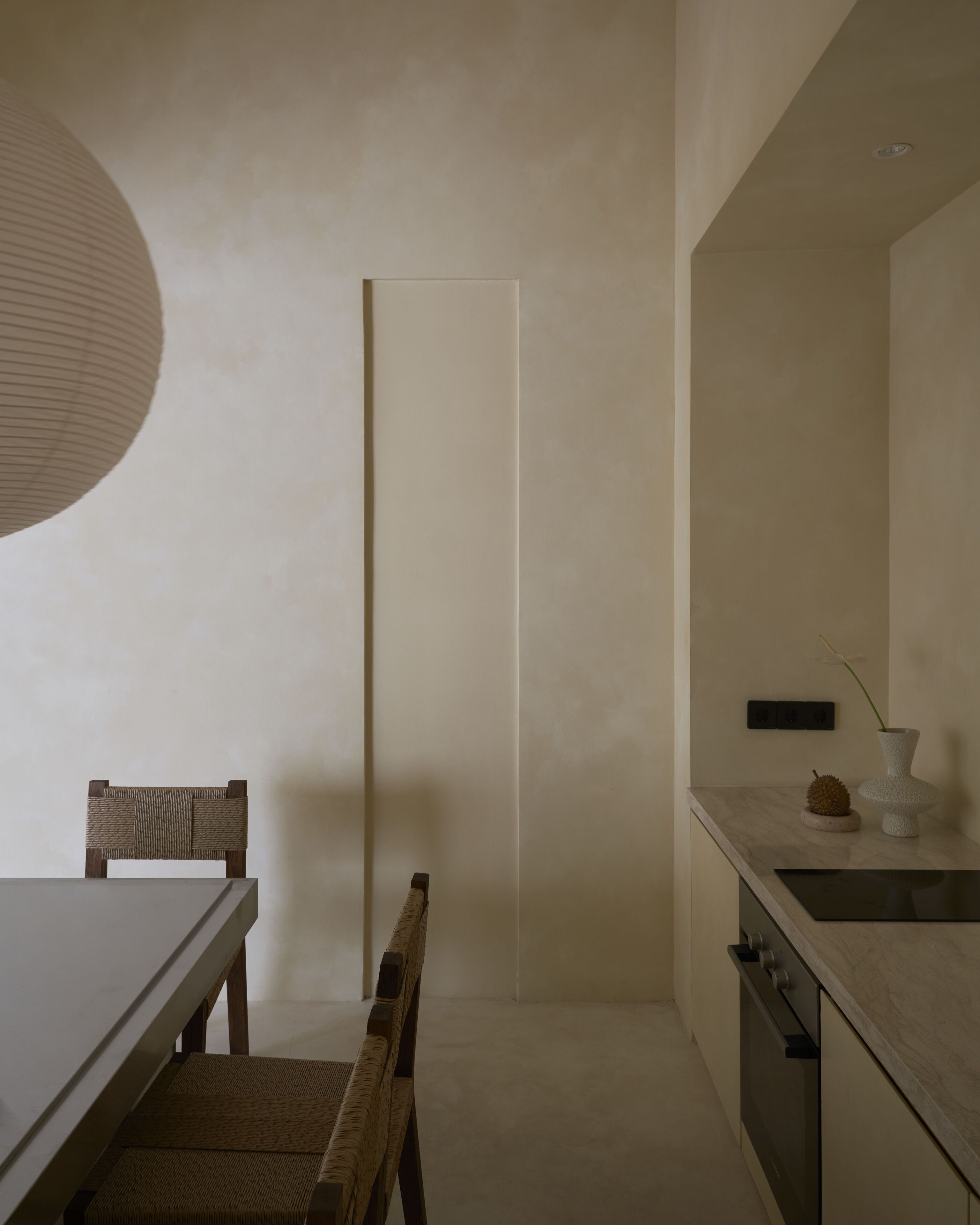A minimalist kitchen with a white table, wooden chair, and a single pendant light.