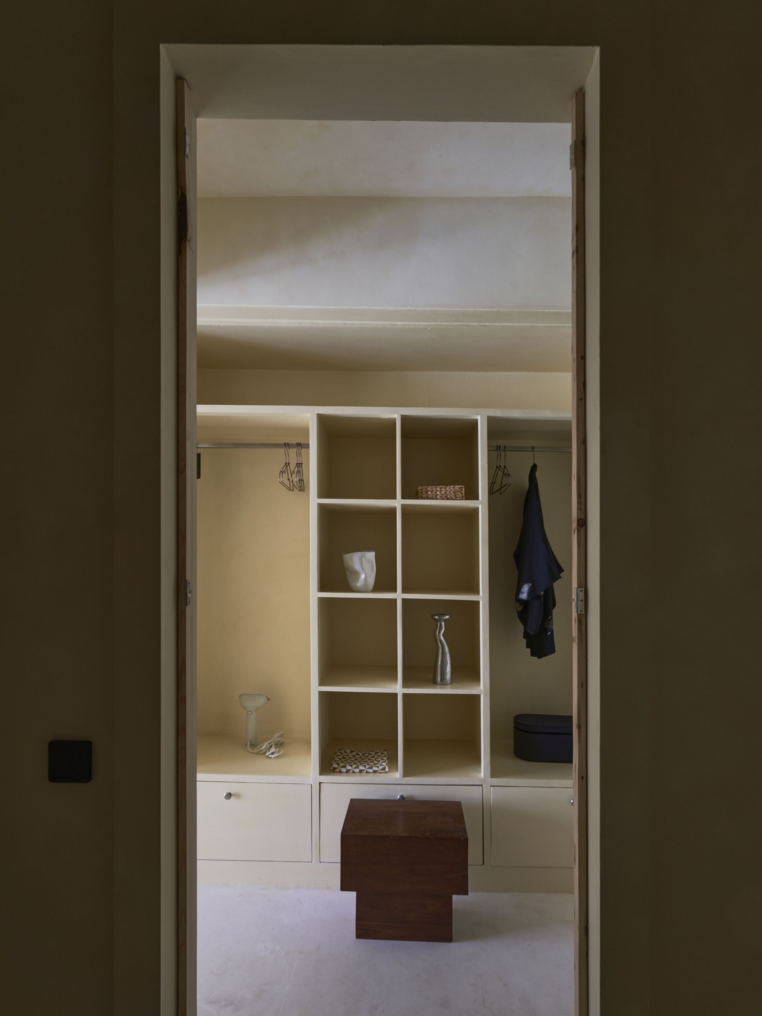 A room with a white wardrobe, a small table, and a bench.