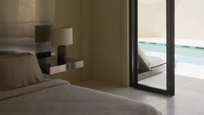 A modern hotel room with a large bed, a bedside table with a lamp, and a view of a pool through an open door. - Tekko Villa Umalas (Kerobokan)