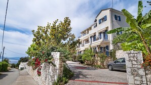 A residential building with a stone wall, a paved driveway, and a car parked in front. - Studio Apartment 'Panorama 2' with Sea View, Wi-Fi and Air Conditioning (Lefkada)