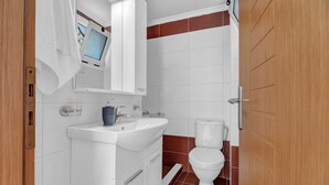 A bathroom with a white sink, mirror, and toilet, wooden door, and a window with a view. - Studio Apartment 'Panorama 2' with Sea View, Wi-Fi and Air Conditioning (Lefkada)