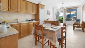 Une cuisine avec des meubles en bois, une table à manger dressée pour quatre personnes et une vue sur l’extérieur grâce à une grande fenêtre.