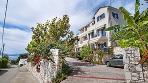 A residential building with a stone wall, a car parked in front, and a clear sky. - Apartment 'Panorama 2' with Sea View, Wi-Fi and Air Conditioning (Lefkada)