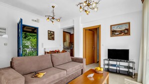 A living room with a sofa, a wooden coffee table, a TV stand, and a door leading to a kitchen. - Apartment 'Panorama 2' with Sea View, Wi-Fi and Air Conditioning (Lefkada)