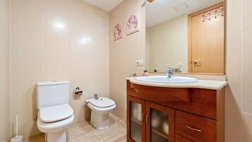 A bathroom with two toilets, a sink, a mirror, and a cabinet.