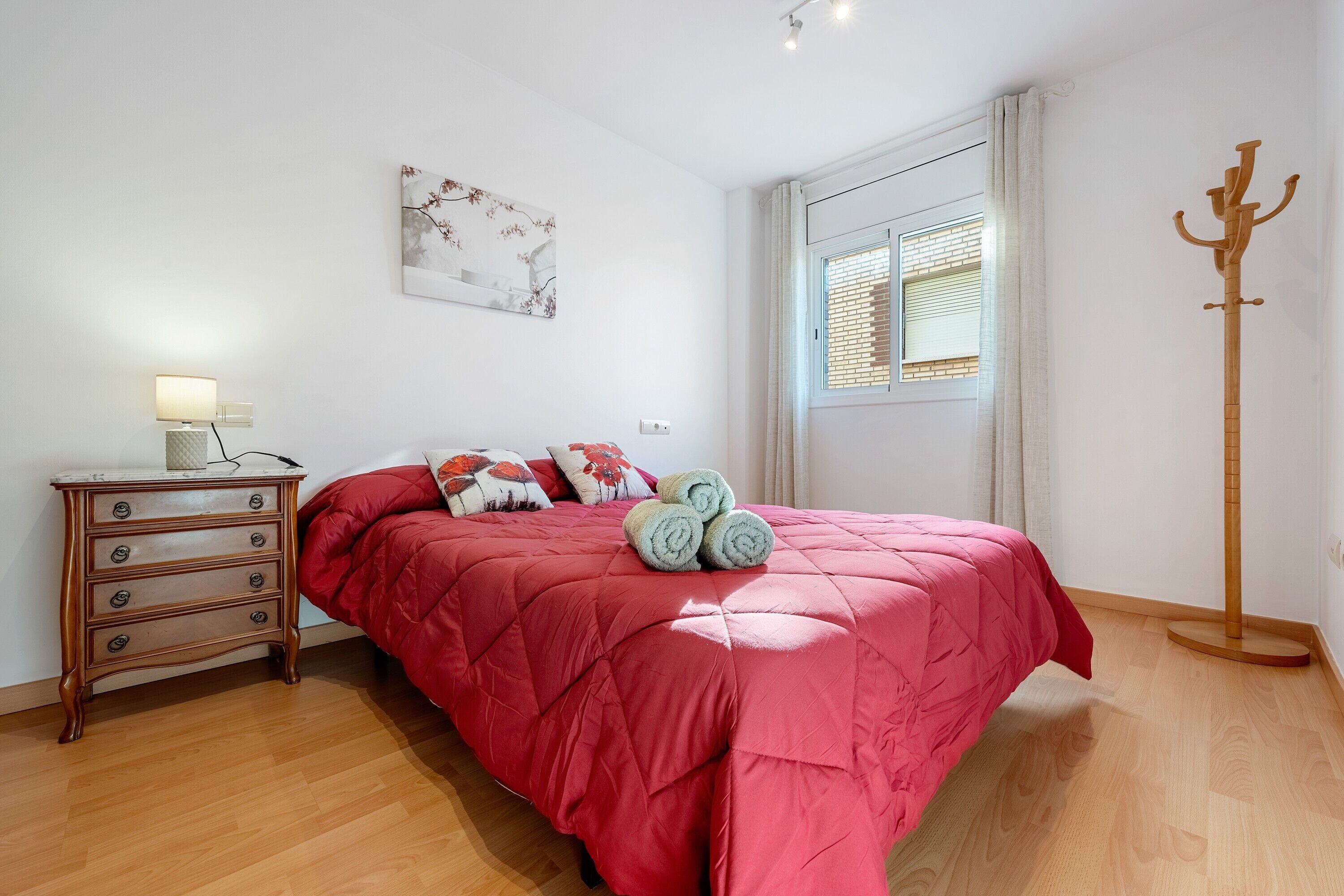 A bedroom with a bed, a dresser, a window with blinds, and a coat rack.