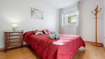 A bedroom with a bed, a dresser, a window with blinds, and a coat rack.
