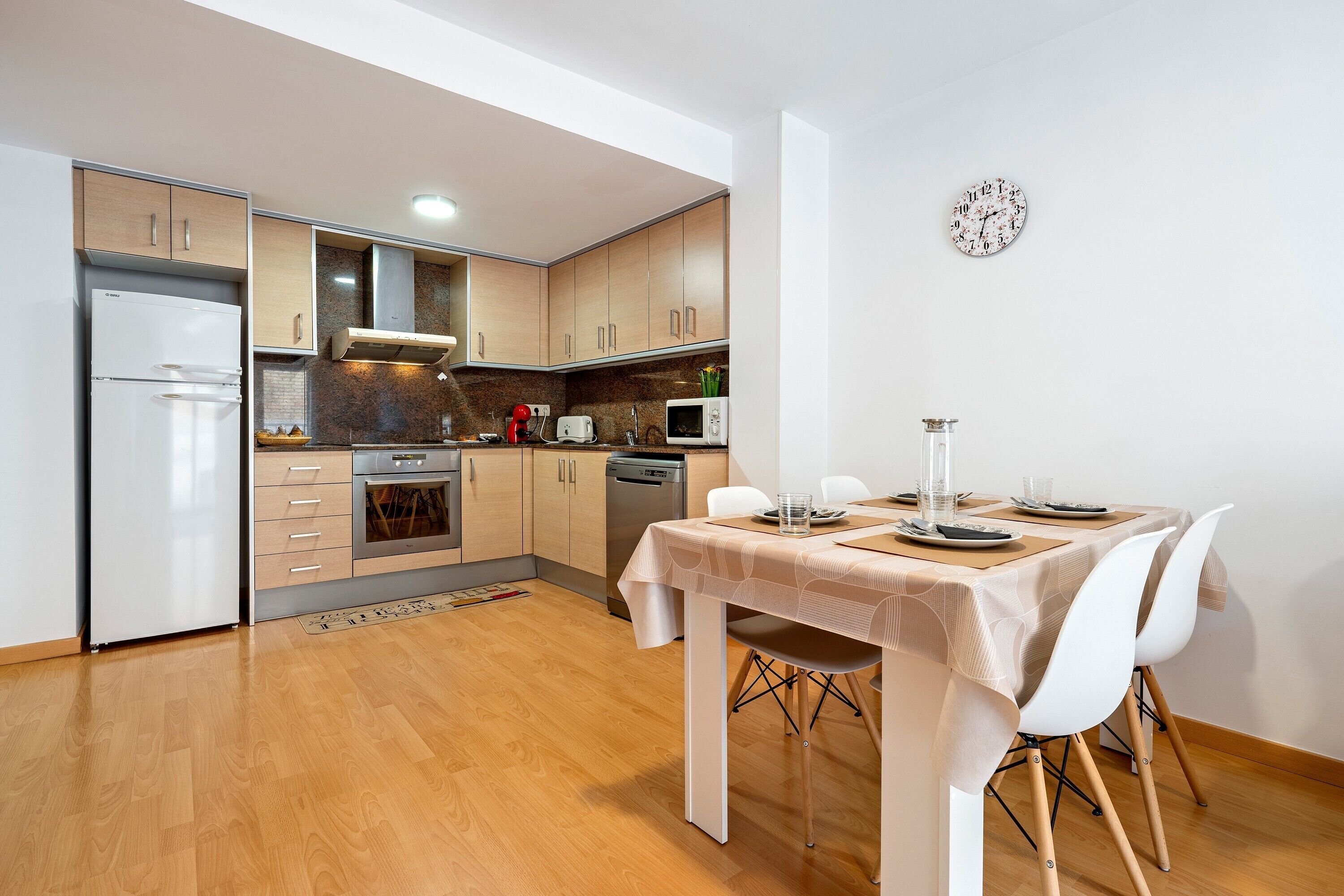 Una cocina moderna con armarios de madera, un refrigerador, un microondas y una mesa de comedor con sillas.