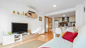 Una sala de estar moderna con un televisor de pantalla plana, un sofá y una zona de comedor con sillas.