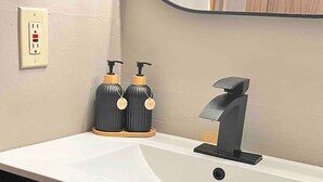 A bathroom with a white sink, black faucet, and two black soap dispensers with wooden handles.