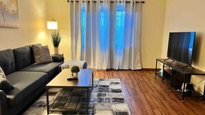 A living room with a sofa, coffee table, TV stand, and a large window with curtains.