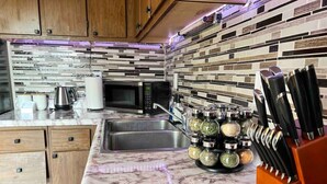 A kitchen with wooden cabinets, a marble countertop, a stainless steel sink, a microwave, and a knife block.