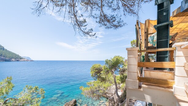 Un bâtiment situé sur la côte, offrant une vue dégagée sur la mer, avec un escalier en bois et un terrain rocheux.