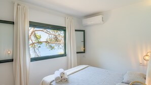 Une chambre à coucher avec un lit, une fenêtre avec des rideaux, un climatiseur fixé au mur et une lampe de chevet.