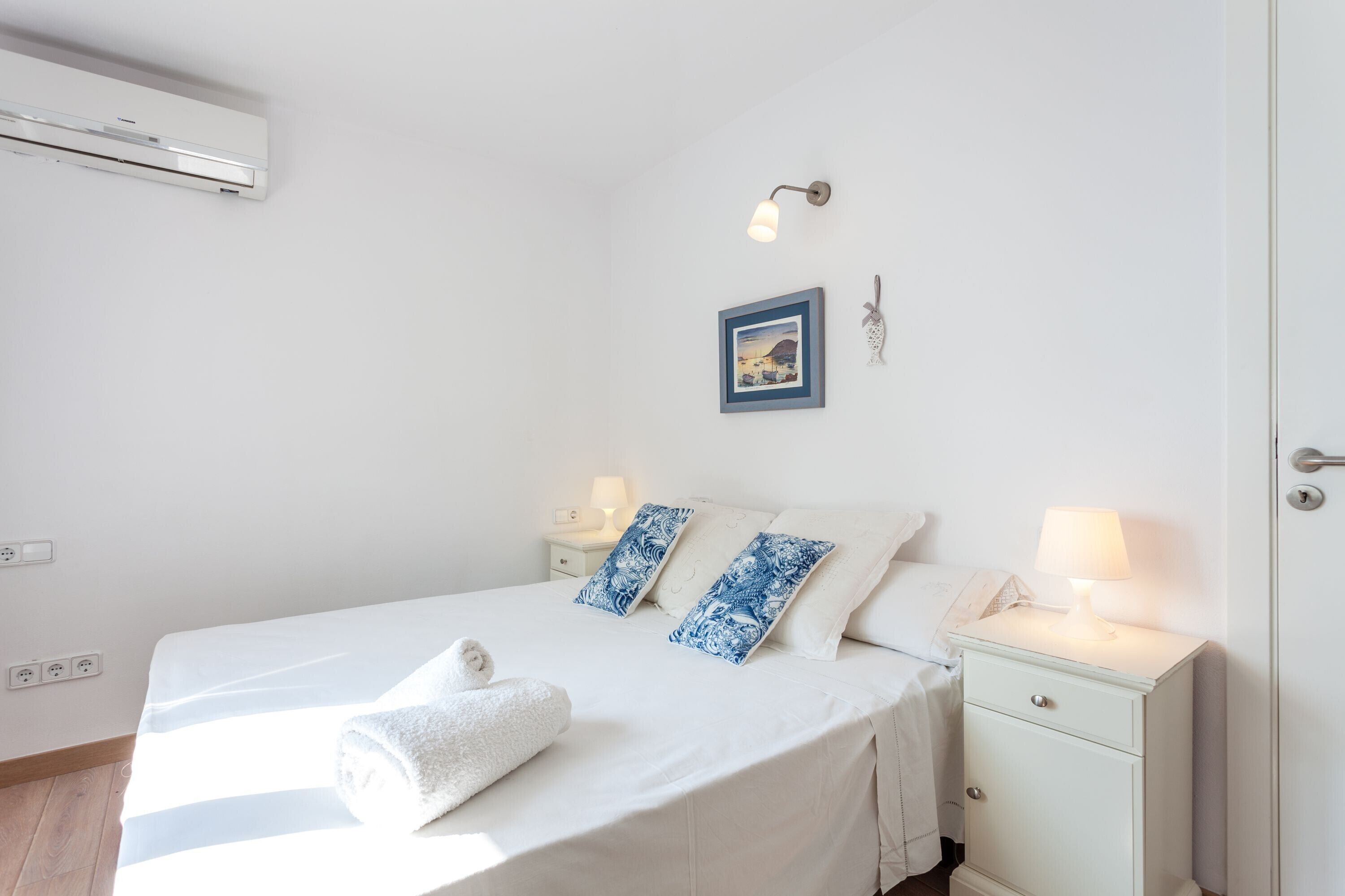 Habitación de hotel con cama, mesitas de noche, aire acondicionado instalado en la pared, un cuadro enmarco y una lámpara de pared.