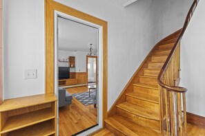 A wooden staircase with a handrail, leading to a room with a sofa and a small table. - Cozy 6 bedroom Entire house in Malden with free parking and WIndow AC (Malden)