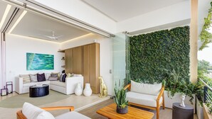 A modern living room with a sofa, coffee table, and chairs. There is a glass wall with a green plant wall behind the sofa. - Designer SoHOPV w/th Ocean Views (Puerto Vallarta)