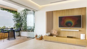 A modern living room with a large TV, a dining area with chairs, a sofa, and a view of the sea. - Designer SoHOPV w/th Ocean Views (Puerto Vallarta)