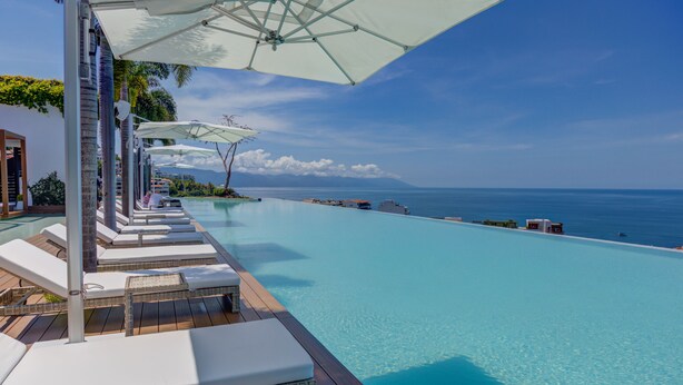 A poolside area with lounge chairs and umbrellas, overlooking a clear blue sea. - Designer SoHOPV w/th Ocean Views (Puerto Vallarta)
