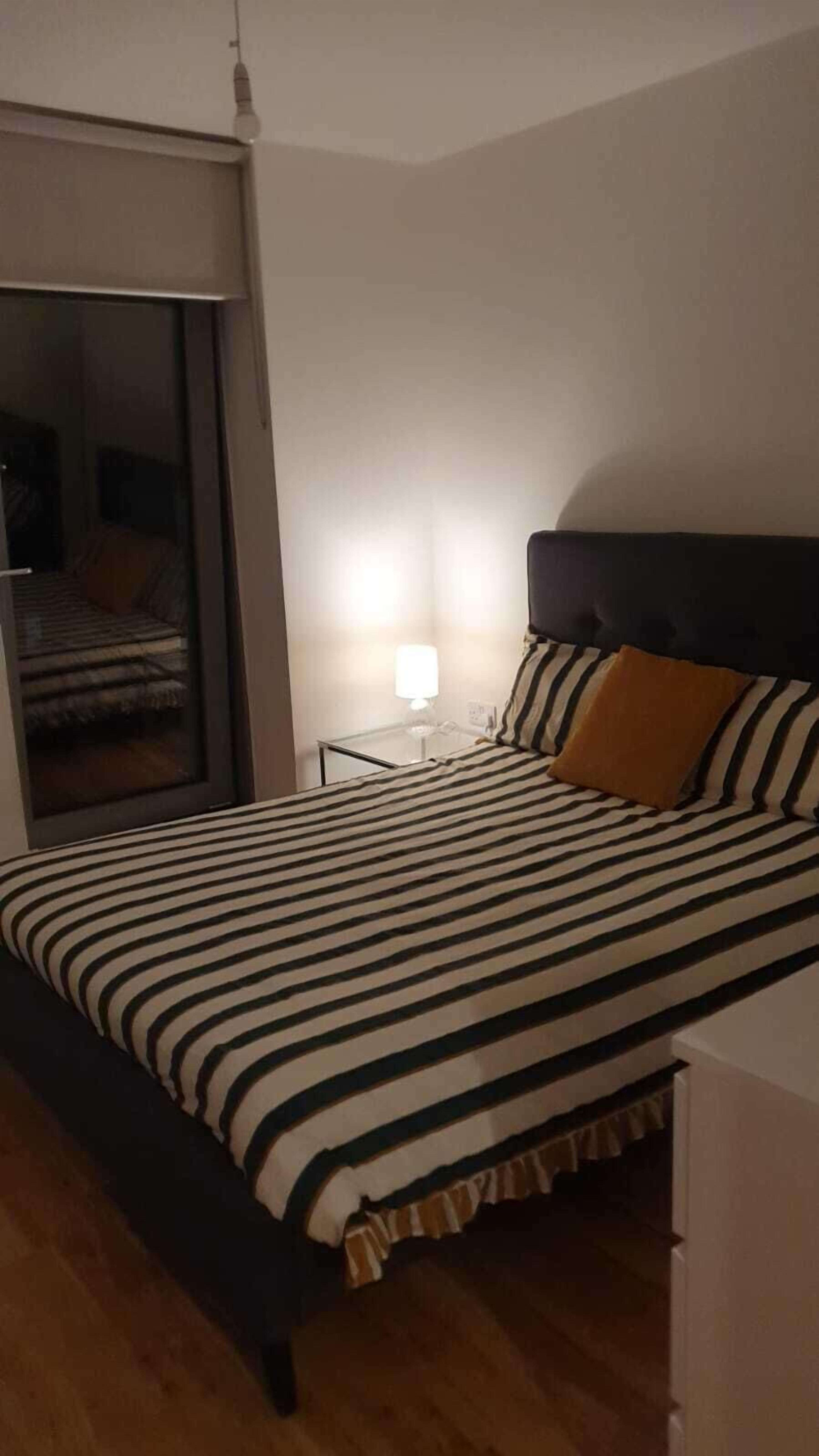 A bedroom with a bed, a nightstand, a lamp, and a sliding door to a balcony.
