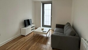 A modern living room with a grey sofa, a white coffee table, and a flat-screen TV on a white cabinet.