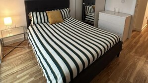 A bedroom with a striped bed, a bedside table with a lamp, a wardrobe, and a mirror.