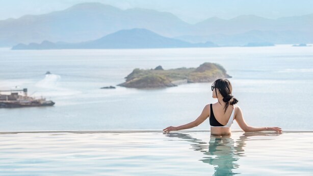 A woman in a bikini at the edge of an infinity pool overlooking a calm sea with distant islands and a clear sky. - ZhouShan Poly Senbo Nature Park and Resort (Zhoushan)