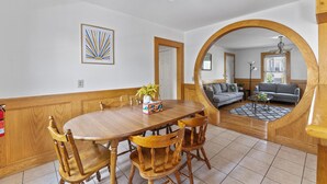 Un coin repas avec une table et des chaises en bois, un miroir au mur et une vue sur le salon.
