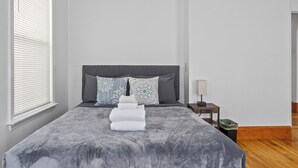 Un lit bien fait, avec une couverture grise, une tête de lit et des coussins décoratifs.
