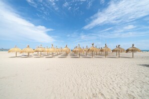 Une plage où des parasols en chaume sont disposés en rangées.