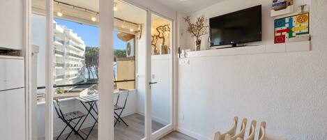 Een moderne woonkamer met een televisie, een eettafel en een balkon met uitzicht op een gebouw.