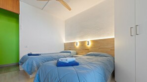 Ein Zimmer mit zwei Betten, einem Holzakustikventilator, einer grünen Wand und einem weißen Kleiderschrank.