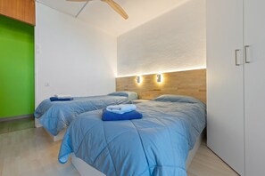 A room with two beds, a wooden ceiling fan, a green wall, and a white wardrobe. - Apartment 'Tirreno 304' with Sea Views, Private Terrace and Wi-Fi (La Pineda)