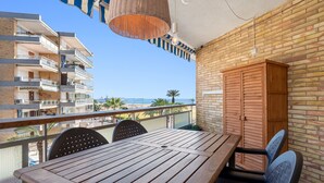 Ein Balkon mit einem Holztisch und Stühlen, einer hängenden Lampenleuchte aus Korbgeflecht, einer Ziegelwand und Blick auf ein Gebäude und Palmen.