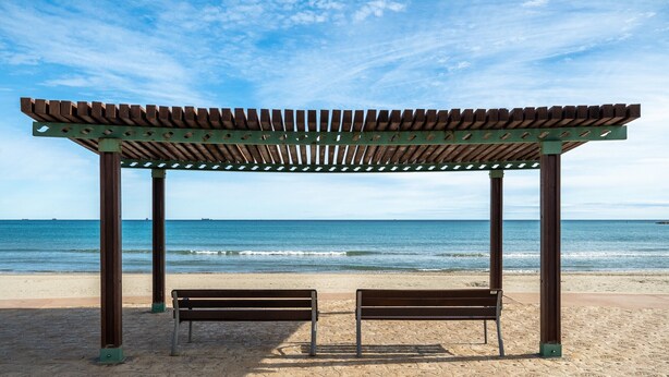 Ein Strand mit einer Holzpergola und zwei Bänken.