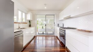 A modern kitchen with white cabinetry, a stainless steel refrigerator, a gas stove, and a wooden floor. - Causeway's Pinnacle! (Yeppoon)