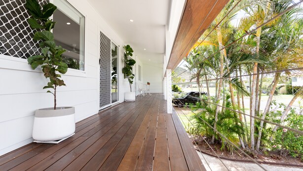 A covered wooden deck with potted plants, a car parked outside, and a view of the surrounding greenery. - Causeway's Pinnacle! (Yeppoon)