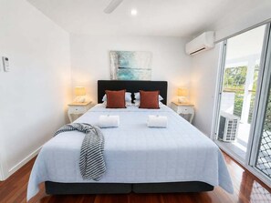 A bedroom with a bed, bedside lamps, a painting, and a view through a window. - Causeway's Pinnacle! (Yeppoon)