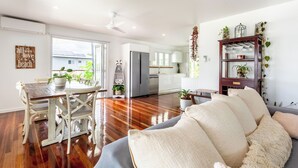 A spacious living area with a wooden floor, a dining table with chairs, a sofa, and a kitchen in the background. - Causeway's Pinnacle! (Yeppoon)