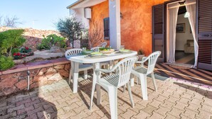 Une terrasse extérieure avec une table dressée pour le repas, entourée de chaises en plastique blanches, et un mur de pierre orné de plantes.