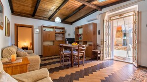 Un salon chaleureux avec un plafond en bois, un coin repas avec une table et des chaises, et une grande porte-fenêtre coulissante donnant sur un espace extérieur.