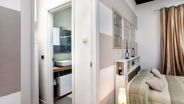 Un dormitorio con cama, mesita de noche, lámpara y vistas al baño.