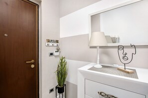 Ein Badezimmer mit Holztür, einem weißen Waschtisch, einem Spiegel, einer Lampe, einer Pflanze und einem an der Wand befestigten Lichtschalter.